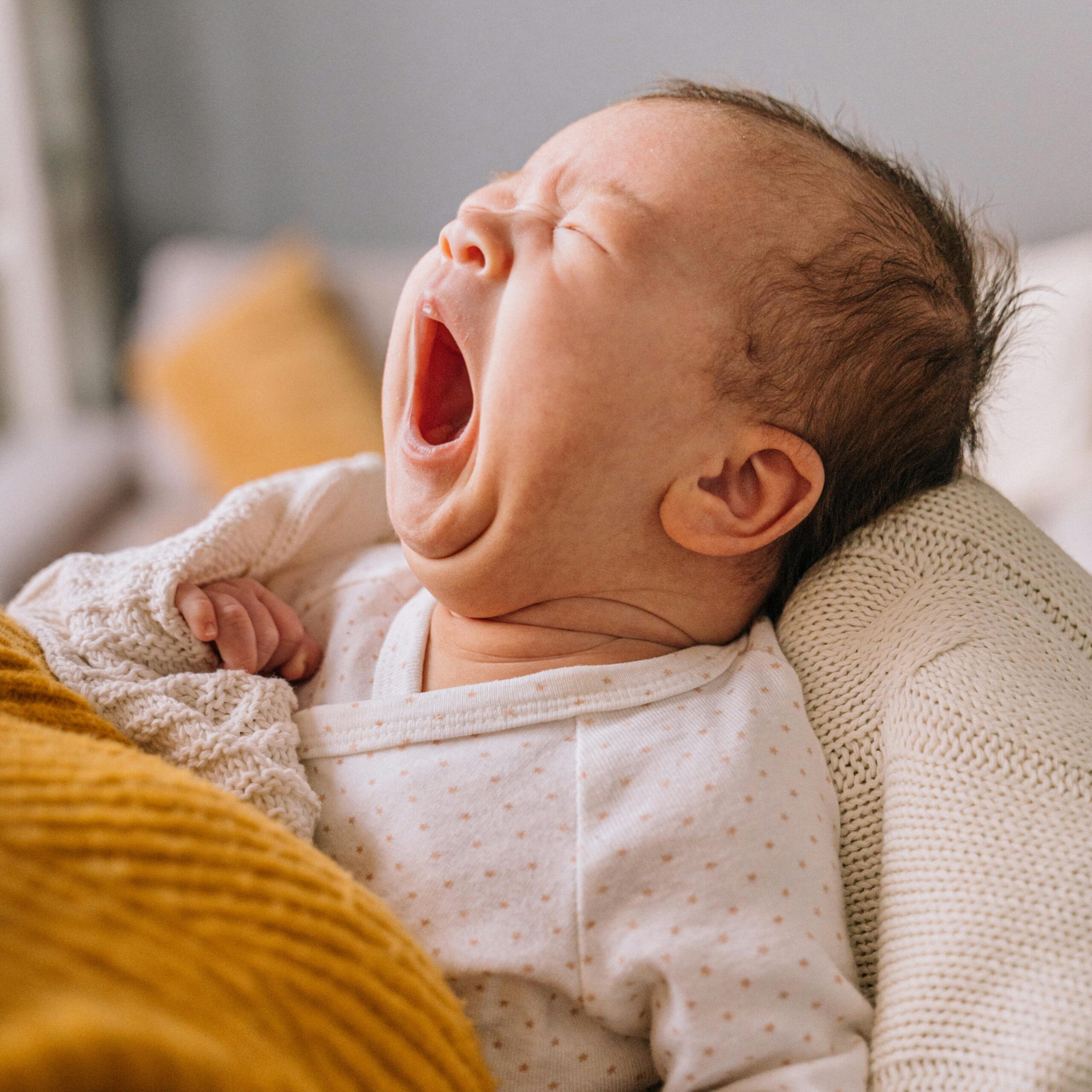 Close-up portrait of a yawning baby in a warm blanket. Perfect for parenting and lifestyle themes.